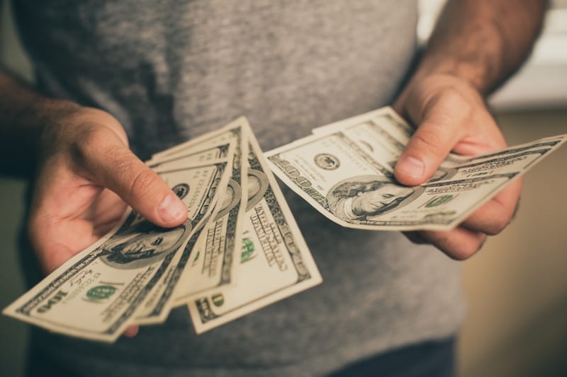 A man in a gray T-shirt holds dollars in his hands.