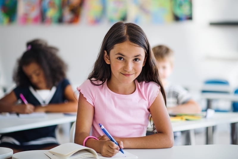 A portrait of small happy school girl sitting at the desk in classroom