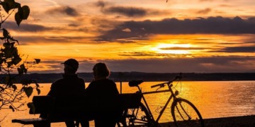 Couple sitting together on a bench watching the sunset, while enjoying the benefits of the Belize QRP Program.