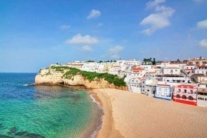 A view of the coast of the Algarve region in Portugal, with blue and green water and bright trimmed houses.