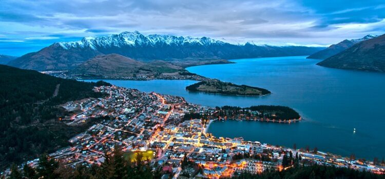 A view over a city in New Zealand at dusk with mountains and water in the background