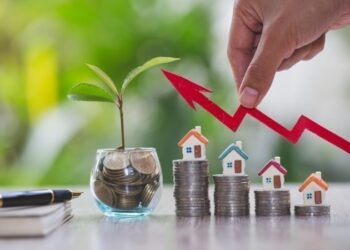 Businessperson's Hand Holding Arrow Over Stacked Coins With House Models. Real estate investment concept.
