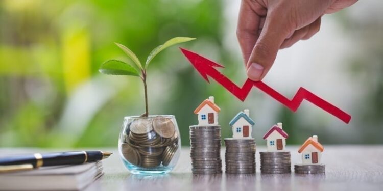 Businessperson's Hand Holding Arrow Over Stacked Coins With House Models. Real estate investment concept.
