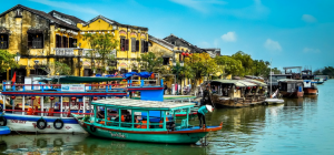 Boats lined up along the river in Hoi An, Vietnam with yellow properties along the bank.