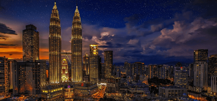 The sun going down over Kuala Lumpur, with building lit up and the Petronas Towers reaching high into the sky.