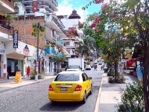 a taxi drives up a beautiful street lined with shops and bougainvillea