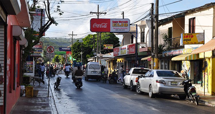 cars and motorbikes on a street lined with shops