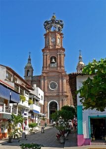 A church at the end of a cobblestone street lined with colorful buildings and trees