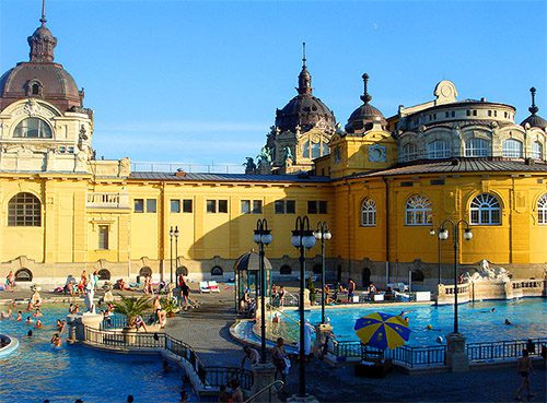 a yellow bath house with many bathers enjoying the pool