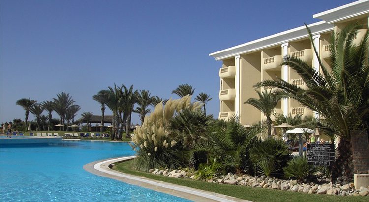 Condo building with pool surrounded by palm trees and tropical landscaping. Guide for buying property in Mexico