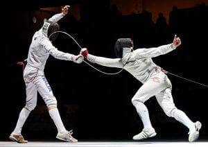 Two athletes dressed in white fencing in a competition