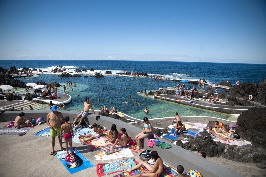 people swimming and lounging by the rock pools of porto moniz
