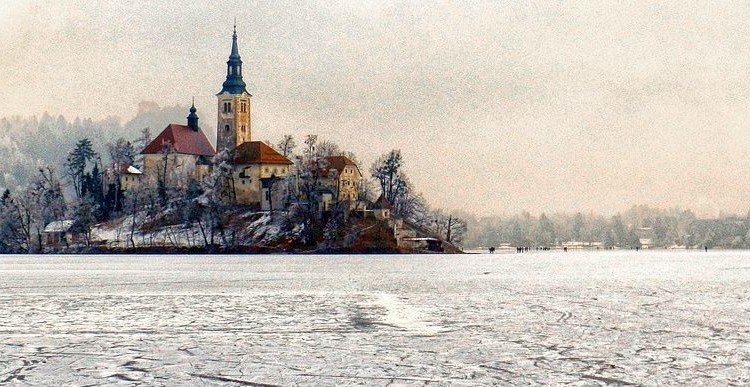a small island with a church covered in show and surrounded by a lake frozen into ice