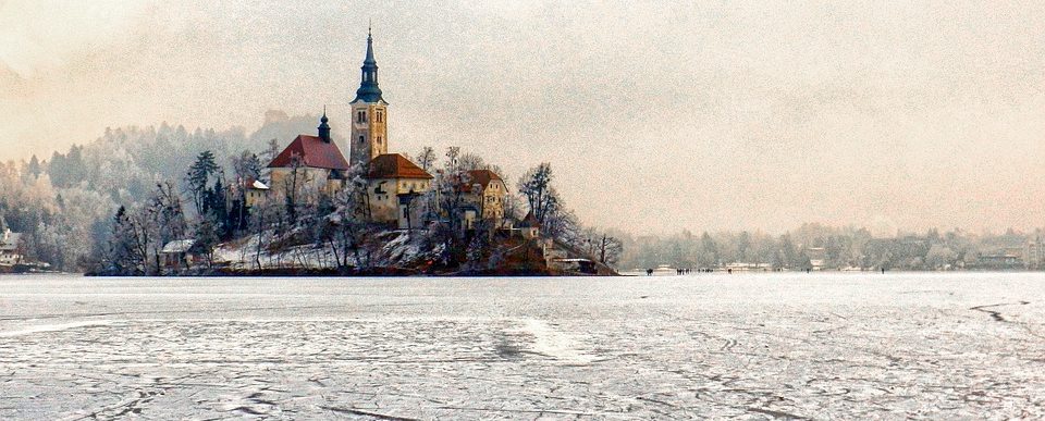 a small island with a church covered in show and surrounded by a lake frozen into ice