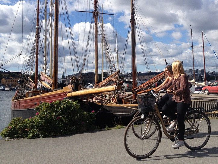 wooden boats docked in Sweden with two young women driving by on a bicycle