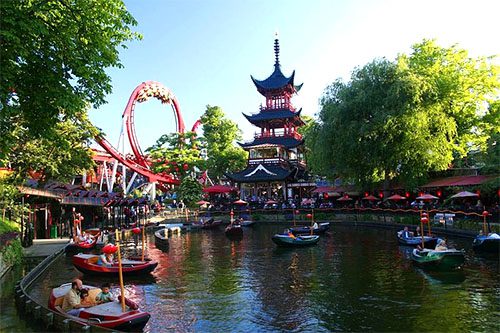 an asian structure, a roller coaster and small boats in a pond at Tivoli Gardens