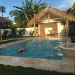 Woman swimming in a pool behind her tropical home.