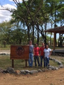 Lief And The Crew At Los Islotes Standing Next To A Wooden Sign That Says Panama Jacks With Tropical Trees In The Background