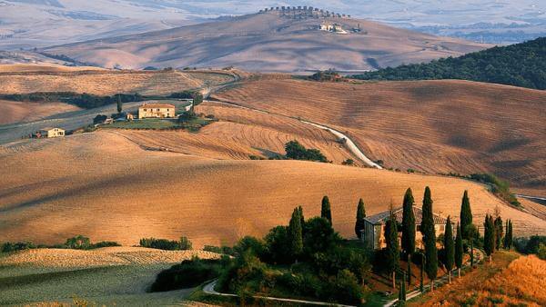 Rolling Tuscany Countryside with farm house, trees and winding roads.