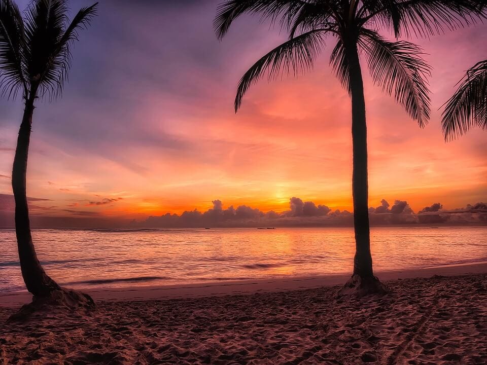 A sunrise as seen from a beach in the dominican republic. The sun is just above the horizon and the sky is pink purple and orange