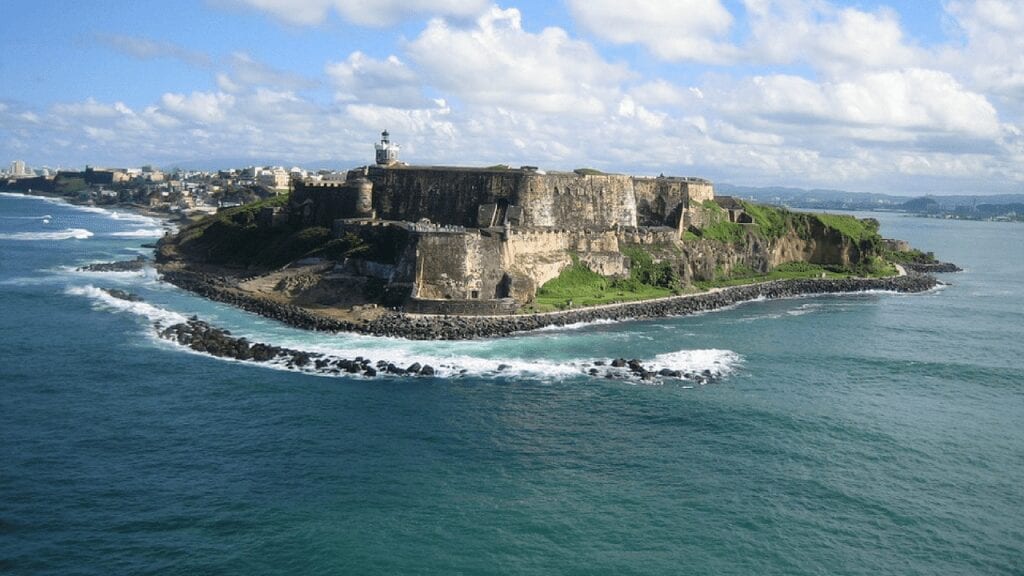 View from the sea of a castle in puerto rico. the castle is massive and you can see along the coaset and also surf breaking over the rocks
