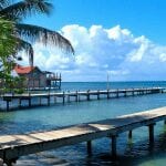 Pontoon in Honduras. palm trees and white sand in the foreground and light blue waters