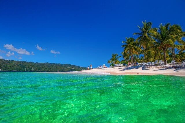The shallow shores of Dominican Republic, with white sands and beach chairs fading down into the green and blue waters.