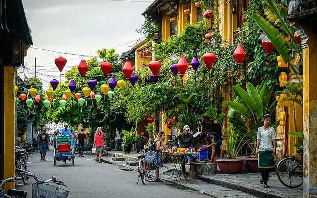 Hoi An Vietnam with yellow buildings and green foliage along a street and colorful lanterns hung over the street.