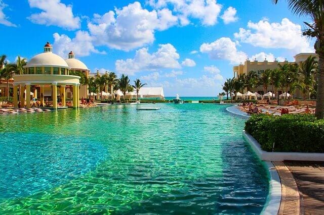 A Mexican resort with green and blue waters splitting the colonial buildings and palm trees to the side.