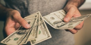 A man in a gray T-shirt holds dollars in his hands. Bank. Casino. Salary. Rates.