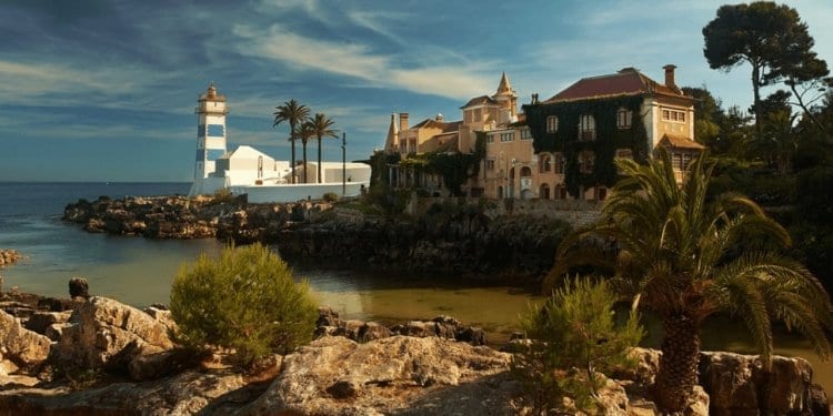 Rocks divided by water, on the other side a lighthouse and houses in front of the ocean in cascais, portugal 