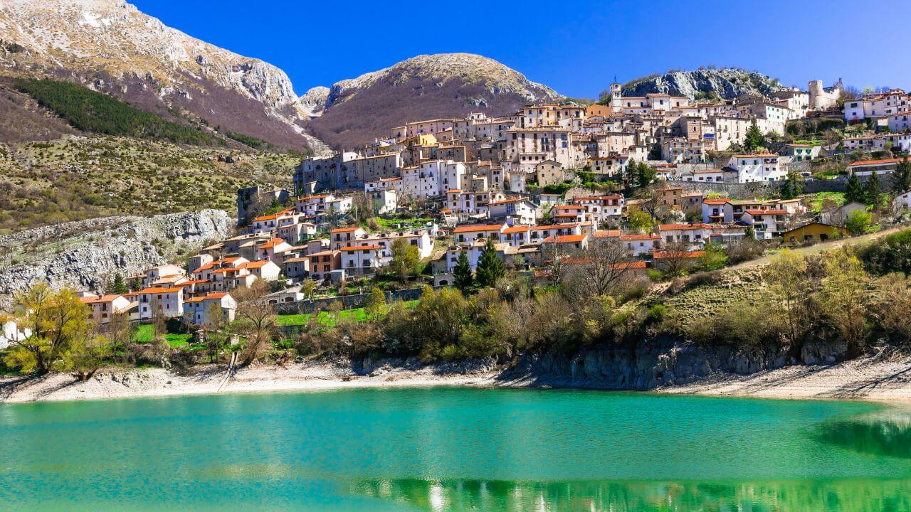 italian town with mountains in background green water in front