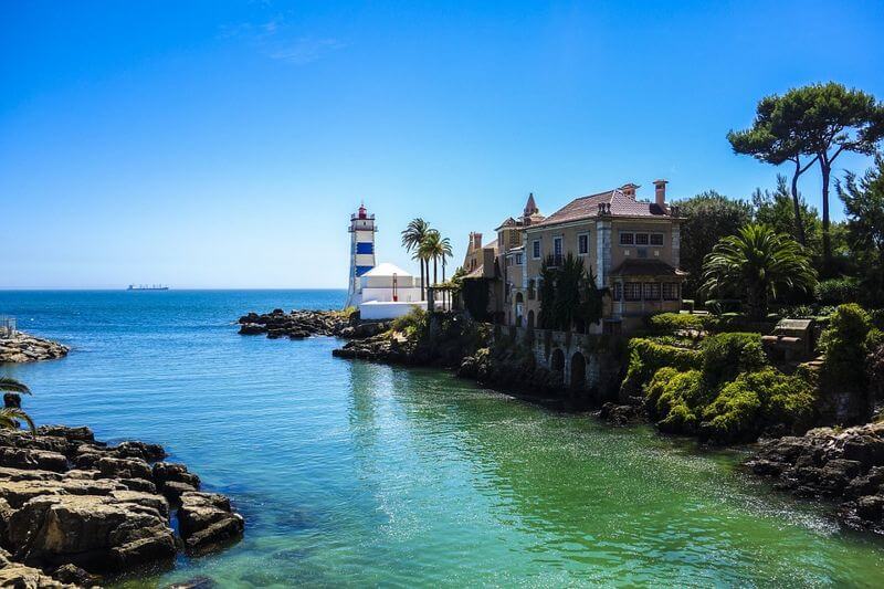 lighthouse in cascais portugal under clear blue skies with clear green waters