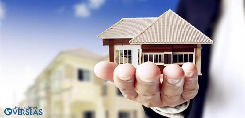 a man wearing a suit holding a tiny house maquette in his hand