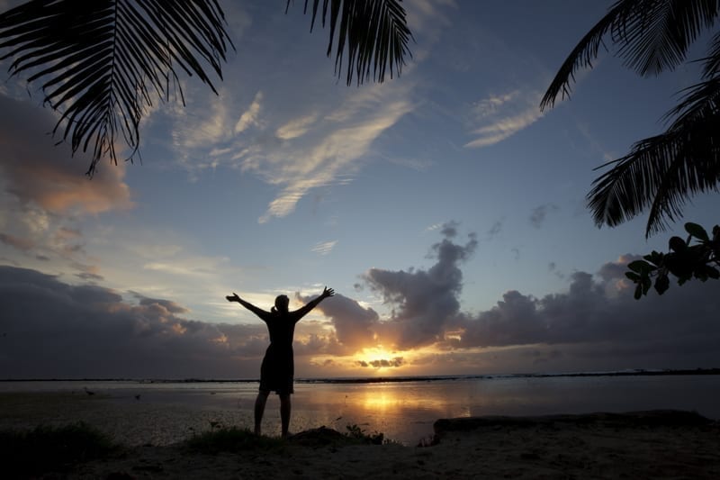 A silhouette of a woman holding her arms out while facing a beautiful sunset.