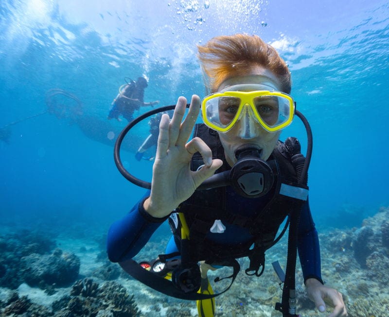 Woman scuba diving in tropical waters making OK hand sign. The Best Places In The World To Scuba Dive