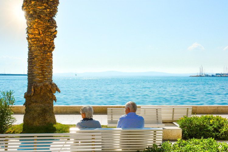 A mature couple sit on a bench and enjoy a view of the Adriatic Sea at the Riva Promenade on the Dalmatian Coast of Croatia.