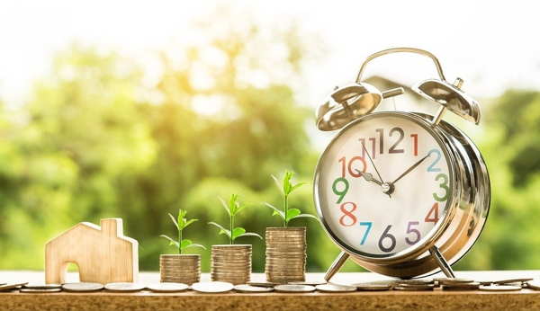 clock next to piles of money with plants growing from them