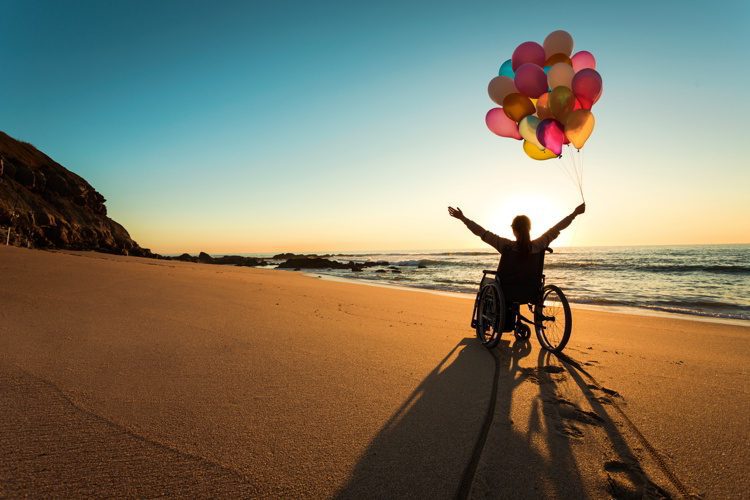 A person on a wheelchair with colorful balloons at the beach. disability friendly countries
