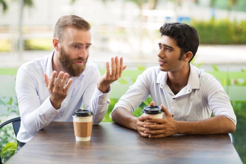 Two male friends drinking coffee and talking in outdoor café