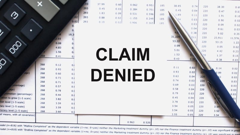  Claim Denied on white sheet with pen, calculator and tables