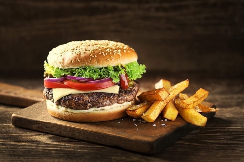 Delicious Hamburger with cheese and french fries on wooden table and dark background. 