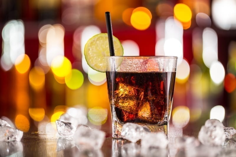 Glass of cola drink on bar counter with ice cubes. 