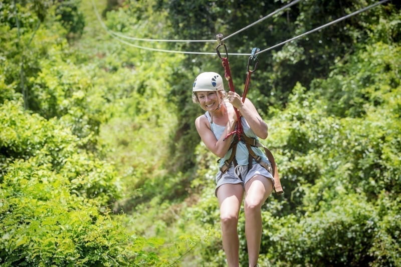 Woman riding a zip line in a lush tropical forest