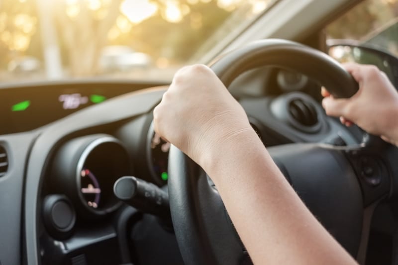 Woman driving her car with both hands on steering wheel. 