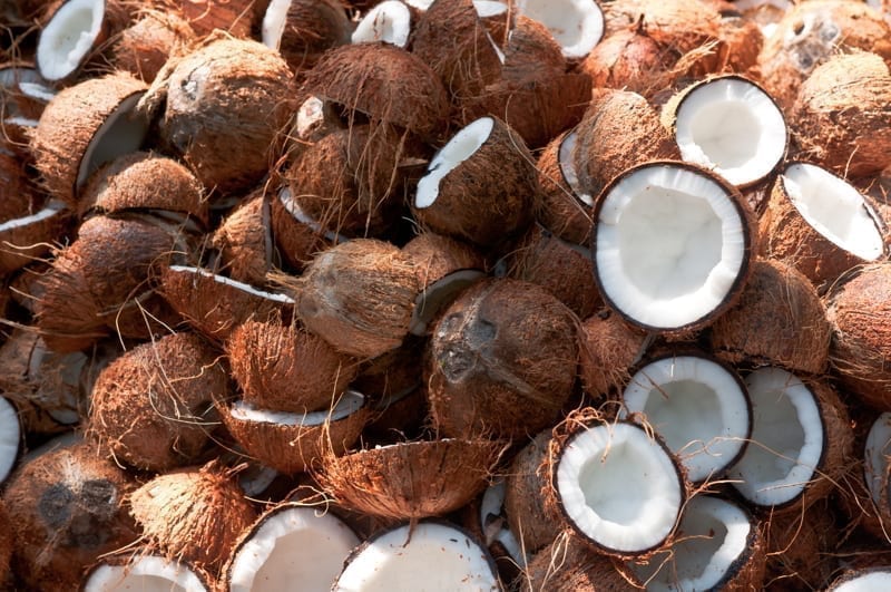 Large pile of Coconuts with one coconut cut open in half. 