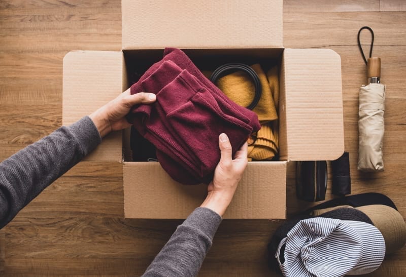 Young person putting accessories clothing in brown box.