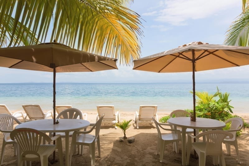 Restaurant tables, sun lounger and beach umbrella under the palm leaves on the beach
