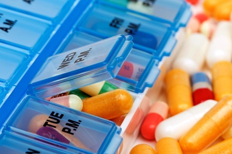 Variety of pills and vitamins in pile beside a pill organizer