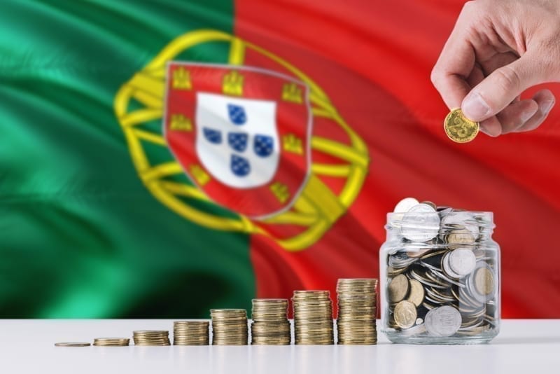 Business man holding coins putting in glass, Portugal flag waving in the background. invest in portugal